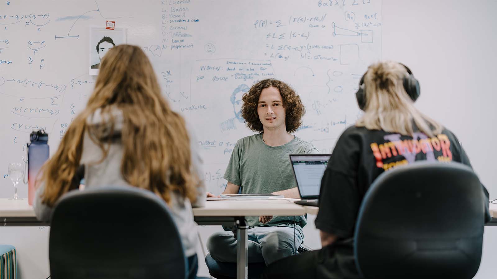 UOW mathematics student Isaac Bankier studying with other students. In the background, a large whiteboard is filled with various equations and notes,