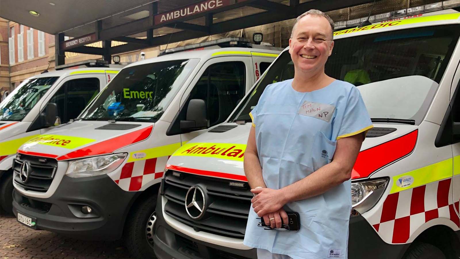 Professor Timothy Wand wearing scrubs standing in front of ambulances.