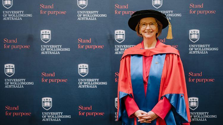 Julia Gillard AC in Honorary Gown in front of navy wall with repeated UOW logo