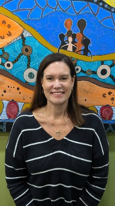 Raychel Davis stands in front of an Aboriginal artwork.