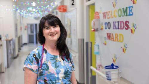 Doctor standing in front of a kids ward. Colourful lettering create a sign.