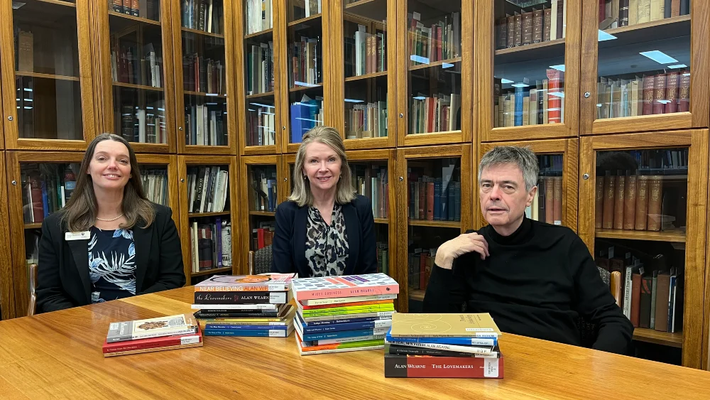 Three people sitting at a table which is piled high with poetry books