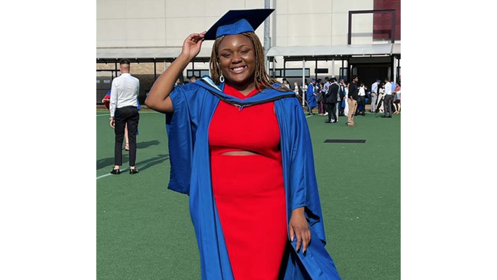 A woman is standing at UOW graduation, wearing a red dress and royal blue gown and hat