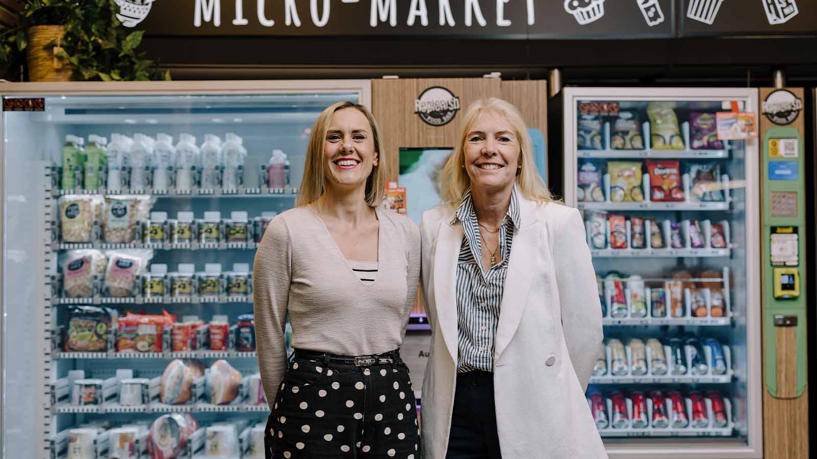 Two women are standing in front of a vending machine