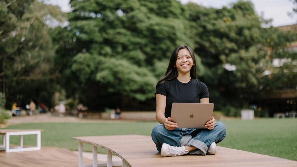 Happy student working on laptop outside on campus