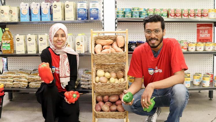 Two people standing in front of shelves stocked with food.