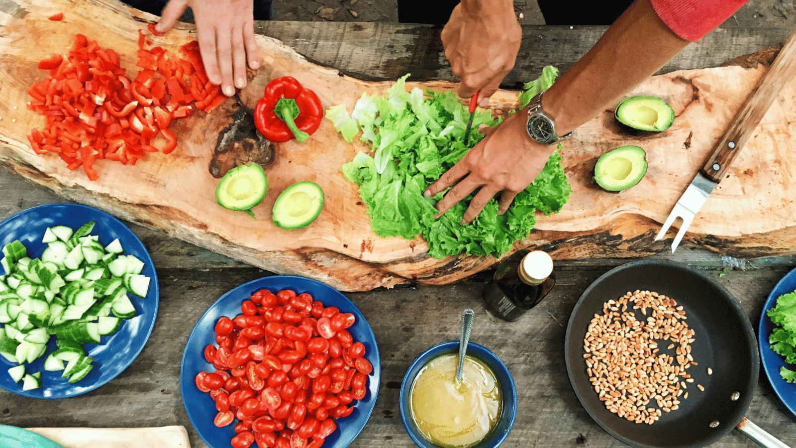 A table of raw ingredients with two people preparing a meal