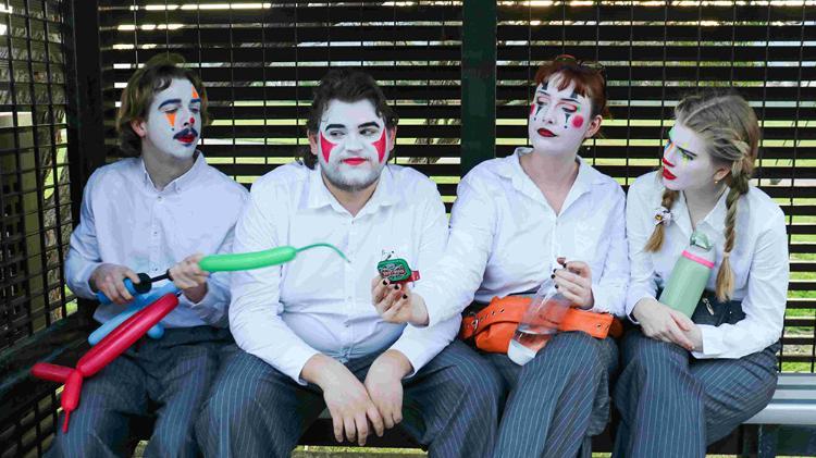 Four students in white shirts have painted clown faces and have balloons