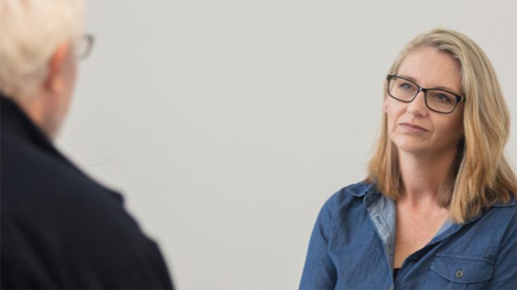 Two people sitting across from each other. The face of one person is visible, while only the back of the other person is in view.