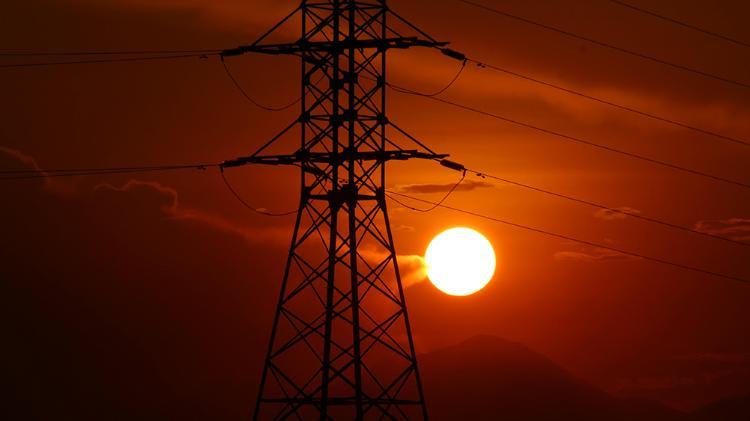 Sun rising over a power tower in foreground and a mountain silhouette in background.