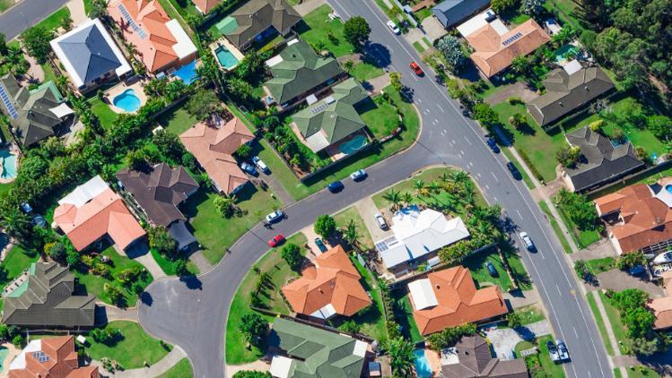 Arial view of a suburban street capturing house roofs, streets, cars and trees.
