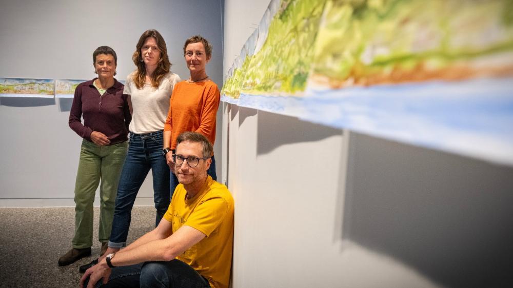 The researchers behind the City+Sea exhibition Kim Williams, Sarah Hamylton, and Leah Gibbs, with Lucas Ihlein in front, with one of the watercolour artworks on the wall next to them. Photo: Paul Jones
