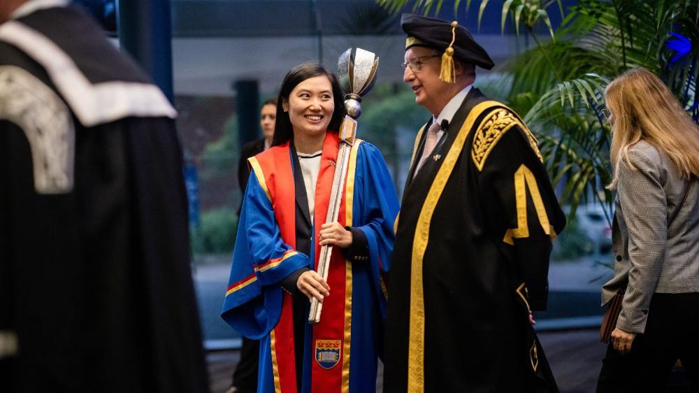 Dr Susan Zhang with UOW Chancellor Michael Still. Dr Zhang is holding the mace, as the official Mace Bearer at the Chancellor's Installation Ceremony in August 2024.