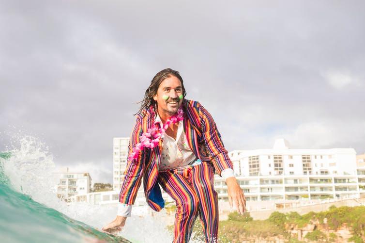A man in a rainbow suit on a surfboard