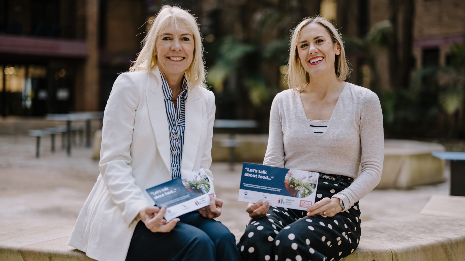 Karen Charlton and Katherine Kent holds the Illawarra Shoalhaven food survey flyer and sit next to each other on a bench. Photo: Michael Gray