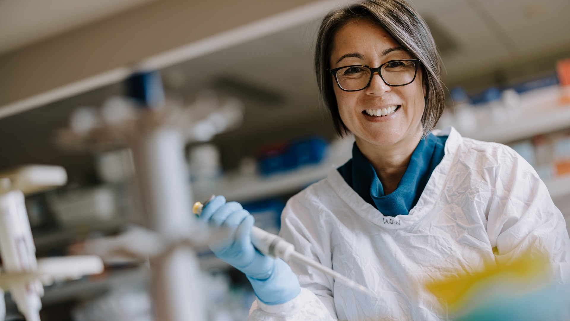 A woman works at a science lab bench in a coat with an array of beakers in front of her. Photo: Michael Gray