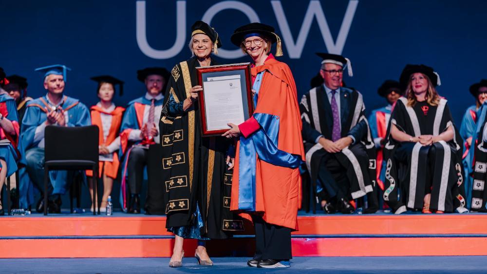 Julia Gillard accepts a framed honorary doctorate on a stage with Deputy Chancellor Nieves Murray. People are seated in the background. Photo: Michael Gray