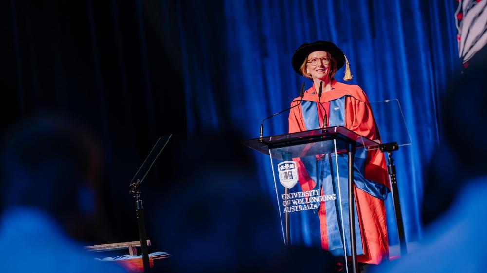 Julia Gillard stands a UOW lectern and delivers a speech on stage at graduation. She wears a graduation cap and gown. Photo: Michael Gray