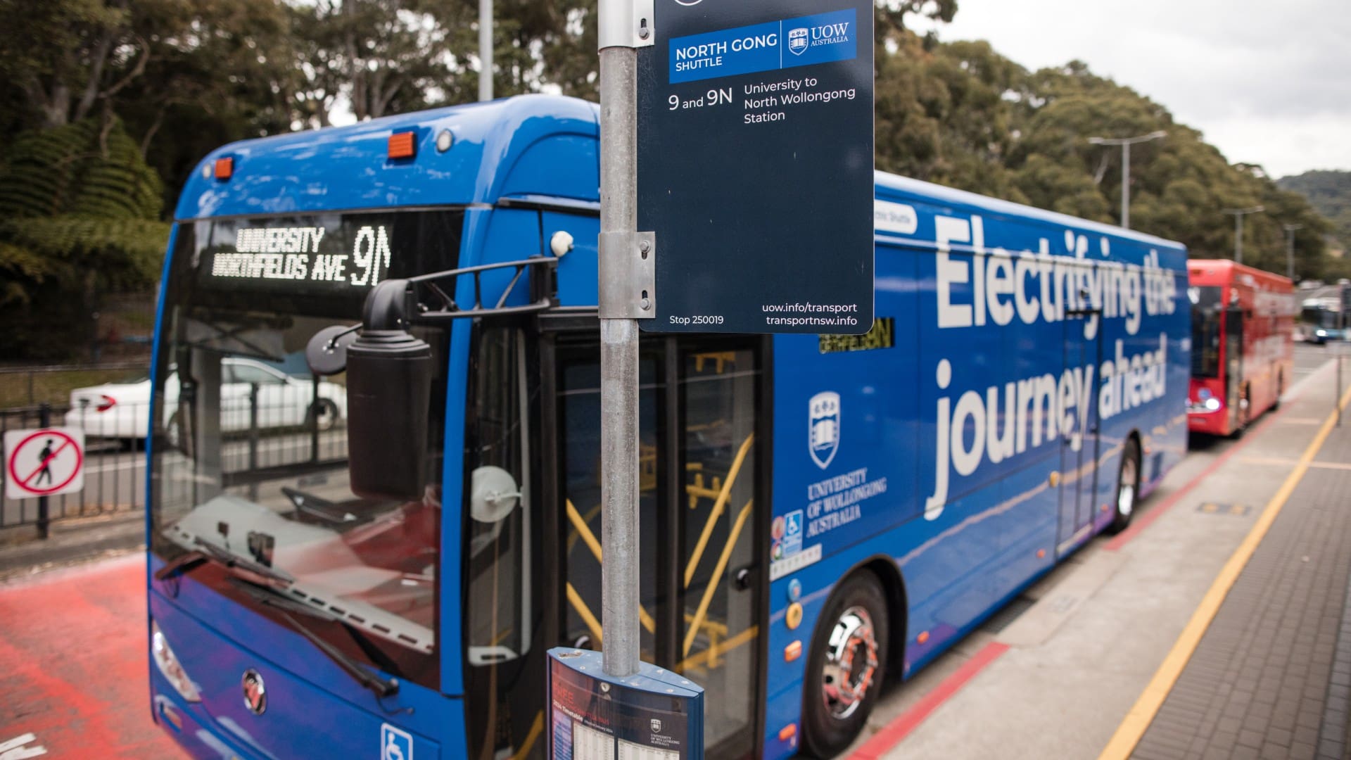 A blue electric UOW bus is parked at the bus stop on Northfields Avenue, with the sign for the shuttle in the foreground. Photo: Michael Gray