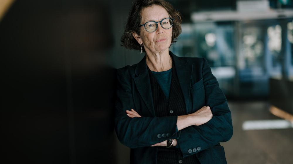Associate Professor Jo Spangaro wears a black jacket and leans against a set of stairs with her arms crossed. Photo: Michael Gray