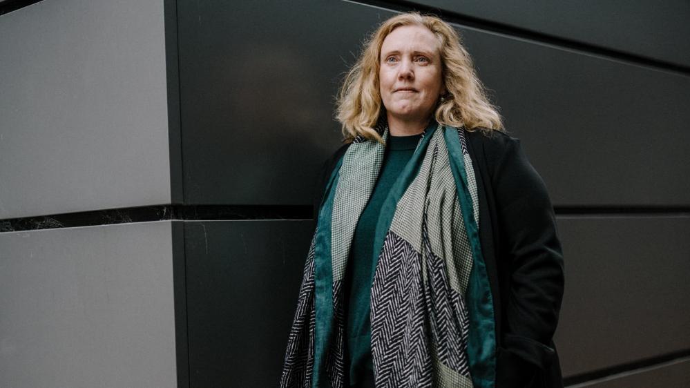 Associate Professor Kelly Lambert leans against a dark coloured wall. She is not smiling. Photo: Michael Gray