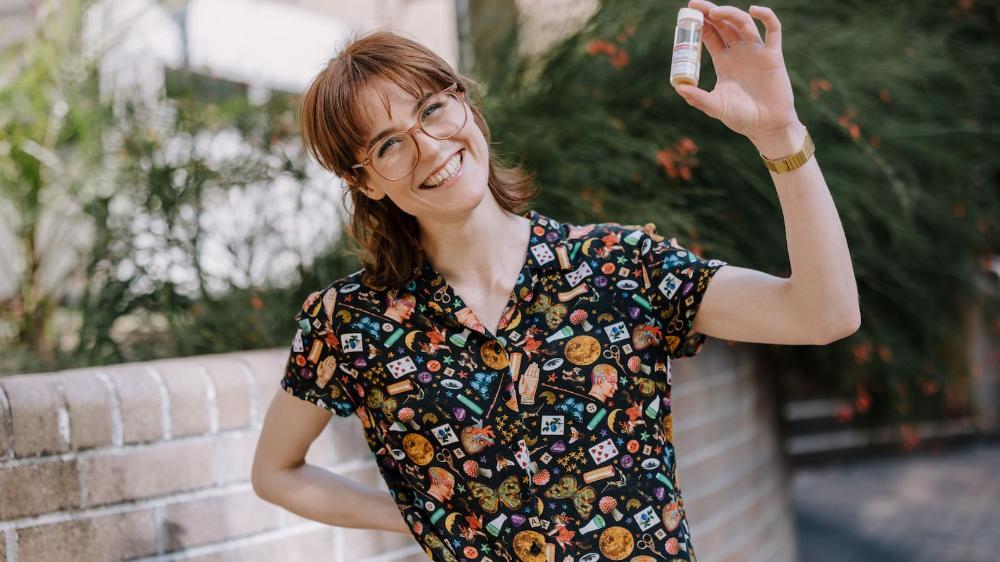 Alice O'Keefe has a big smile and stands in front of the Molecular Horizons Building. She is holding a small test tube.  She wears jeans, a black shirt, and glasses. Photo: Michael Gray