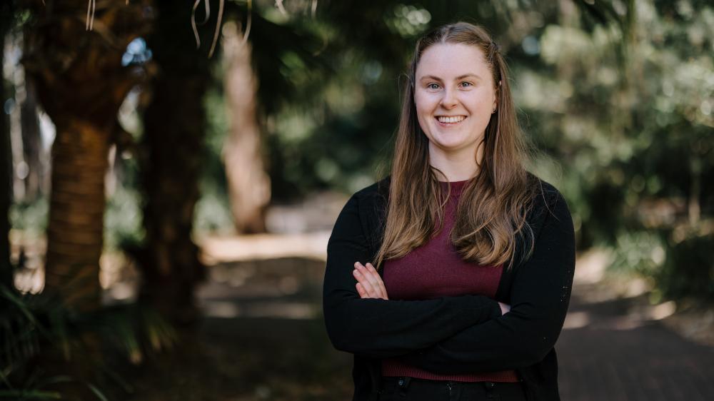 Rebecca Ryan smiles with bushland in the background. She wears a maroon shirt and black cardigan. Photo: Michael Gray