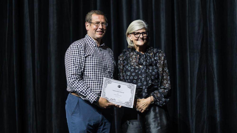 A man stands on a stage and receives a certificate from a woman. They are both smiling. Photo: Ben Calvert Photography