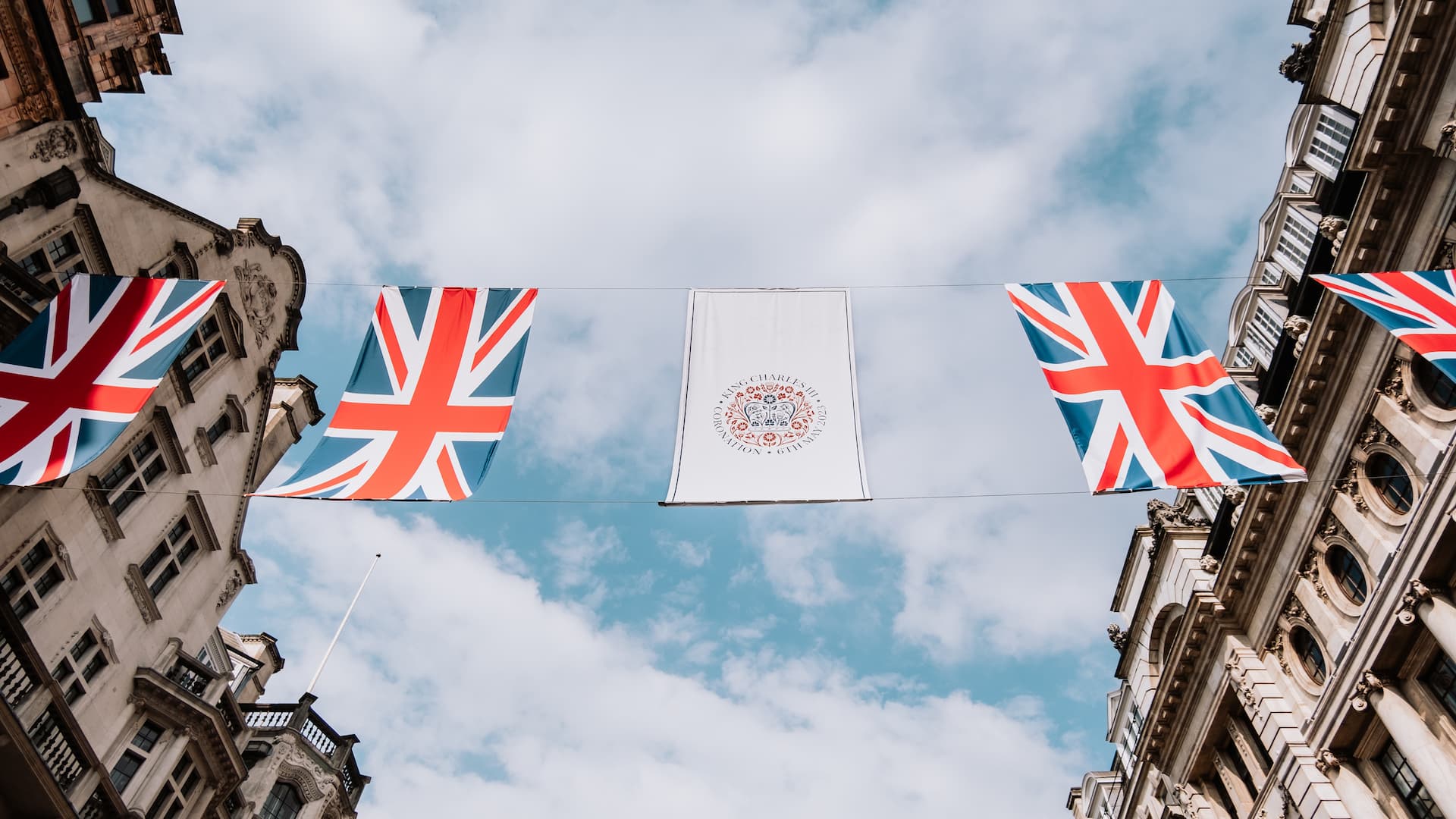 Union Jack flags are strung between two buildings, with the blue sky in the background. Photo: Unsplash